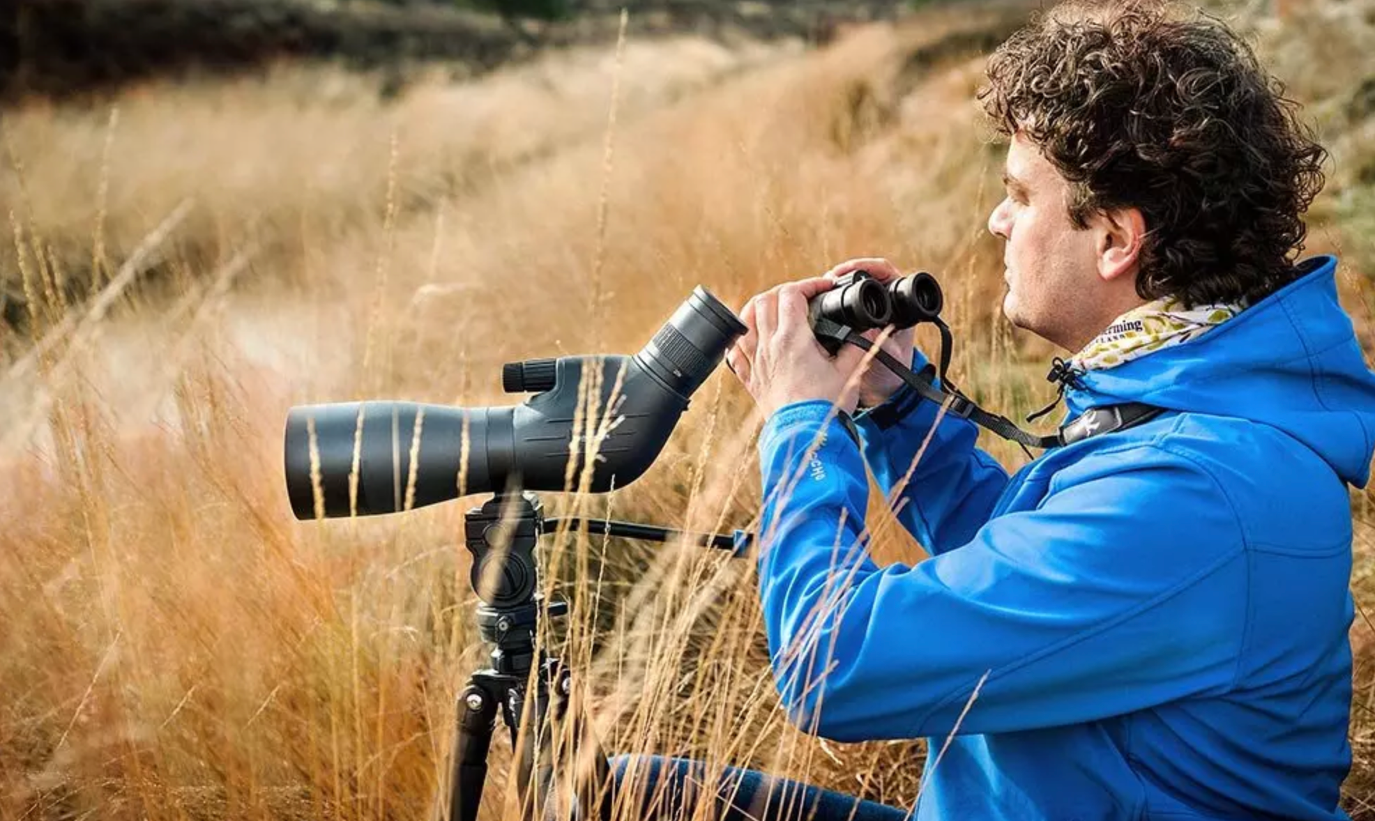 Man in de duinen met een telescoop op een statief en een verrekijker in de hand