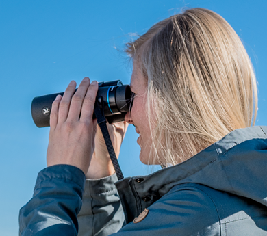 Vrouw met verrekijker in haar hand naast een verrekijker statief, op zoek naar vogels